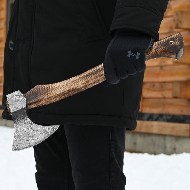 Person holding a handmade axe with a wooden handle outdoors in winter