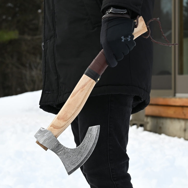 Person holding a large hand forged axe in a snowy outdoor setting