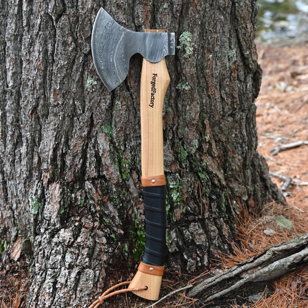 Axes with leather sheathes against a tree in a forest setting