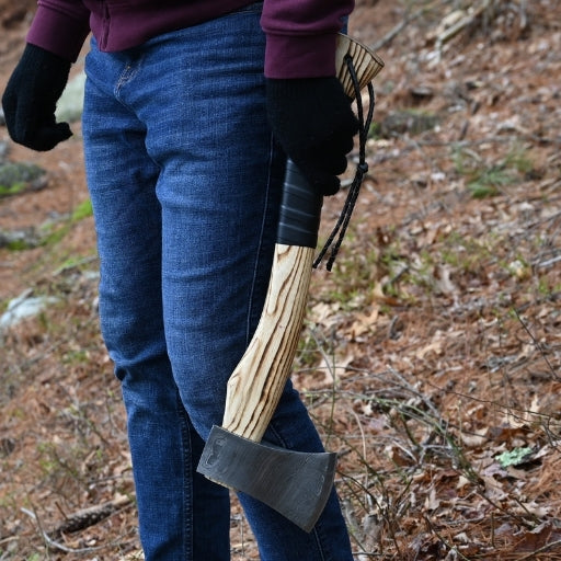 Person holding a handmade axe with leather wrap on handle in a forest setting