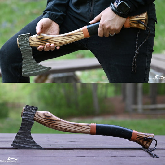 Person holding a wooden-handled axe with a black blade, outdoors.