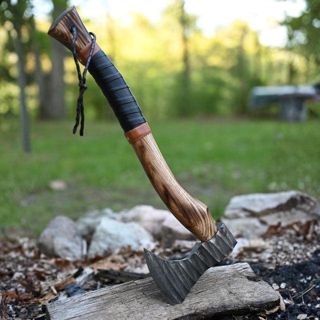 Wooden-handled damascus steel axe with leather wrap on a log with a forest background