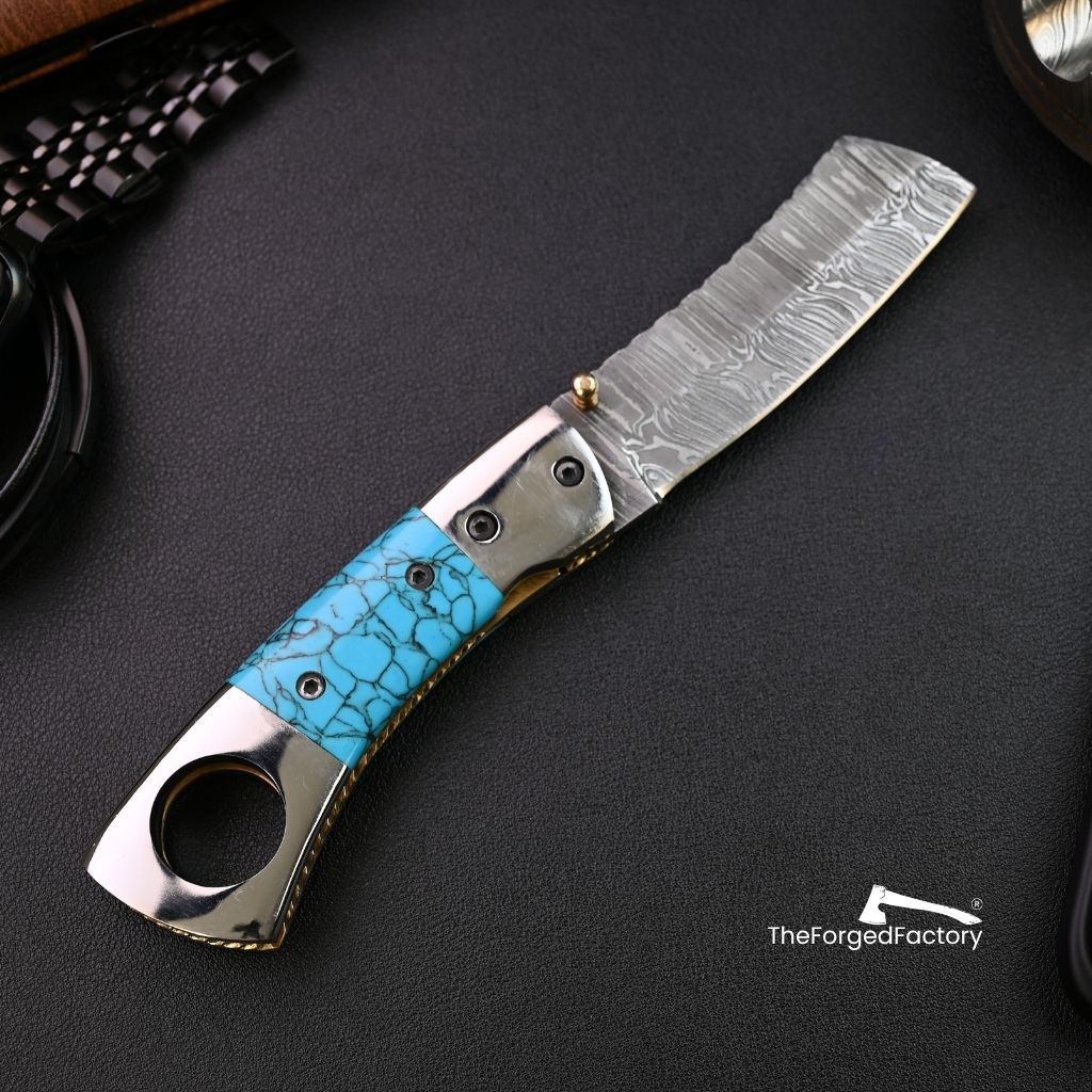 Foldable cigar cutter knife with turquoise handle on a dark surface, branded 'TheForgedFactory'.